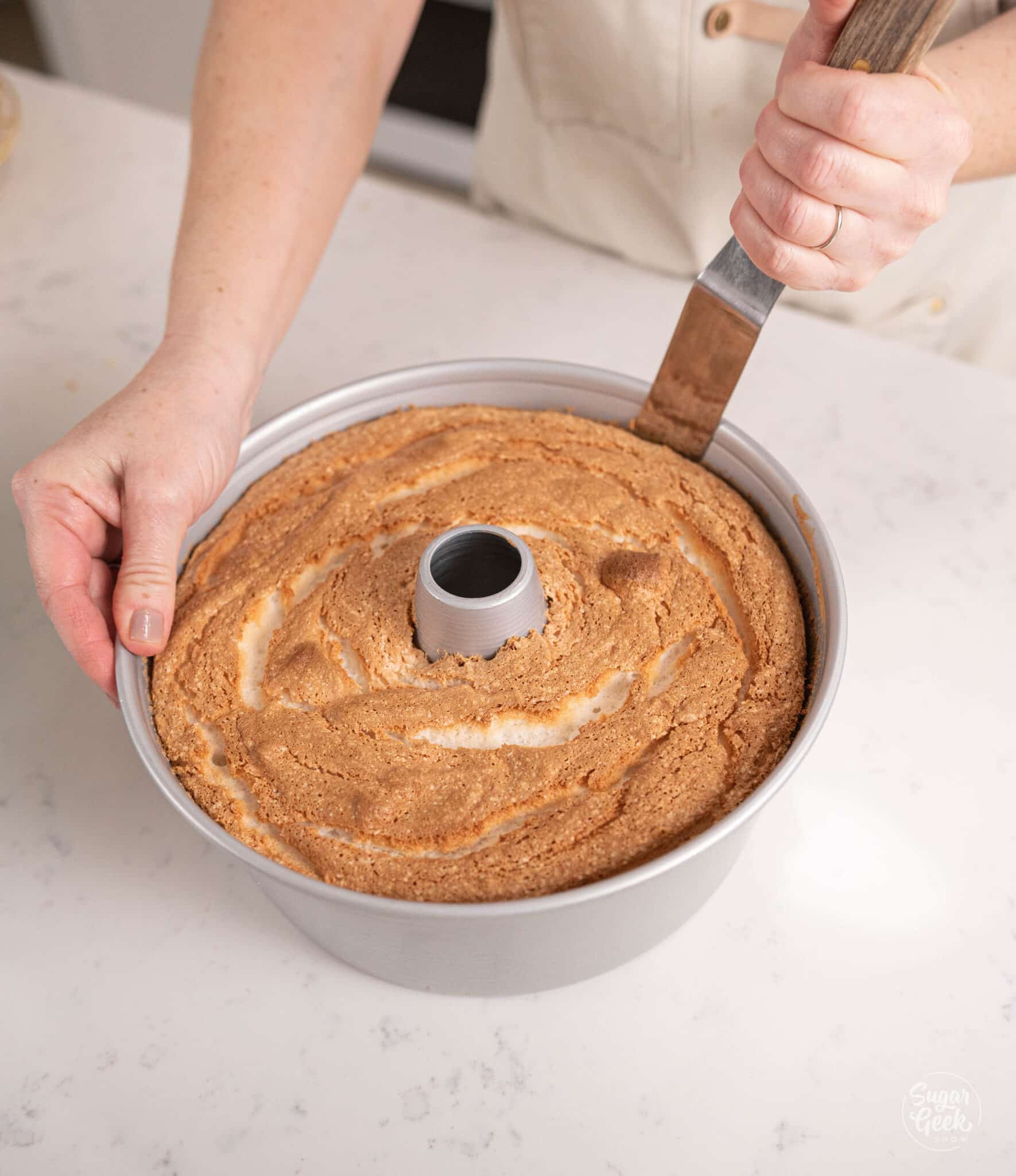 sliding a knife around the edges of an angel food cake in the pan