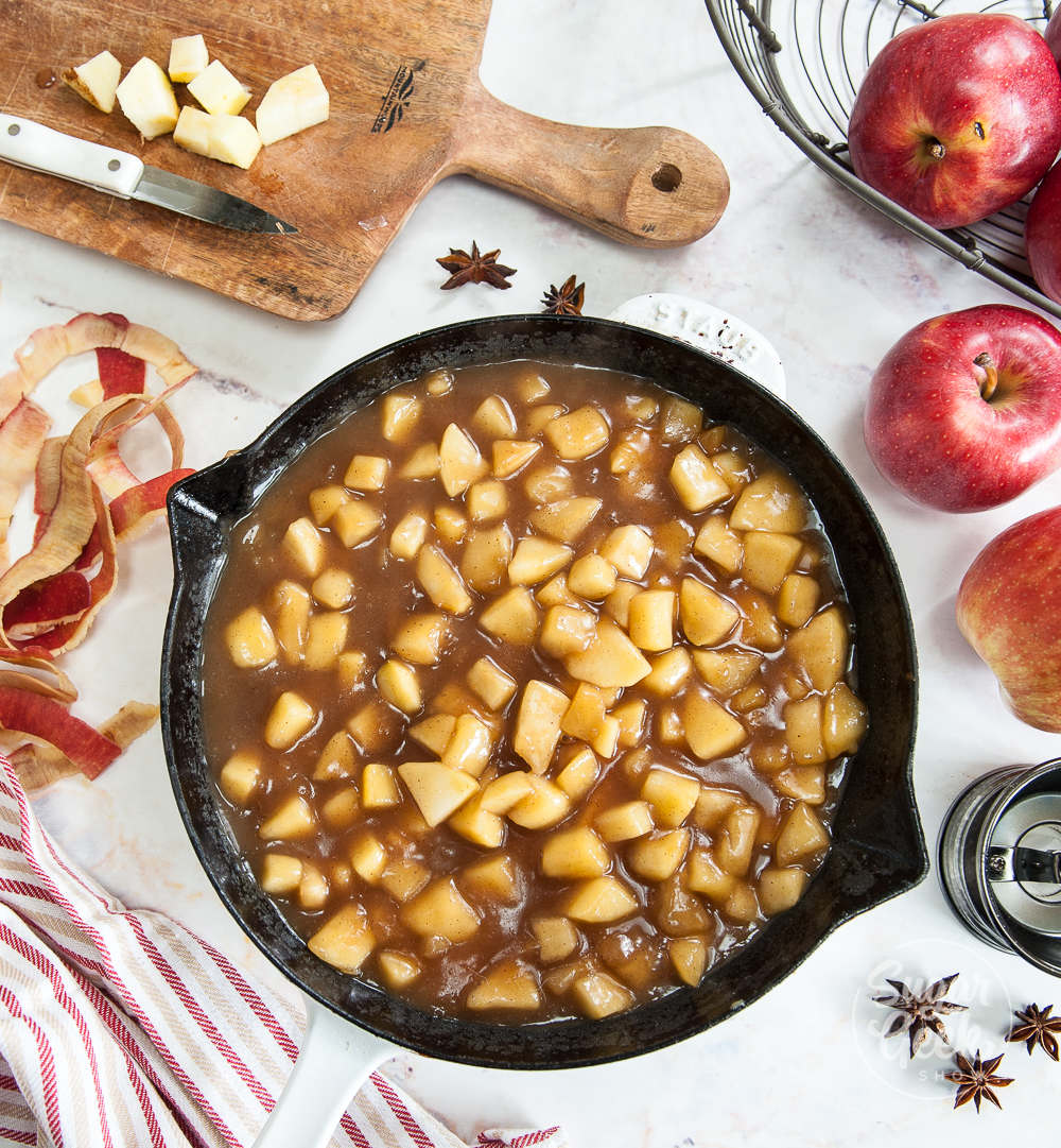 top view of apple filling in a cast iron pan surrounded by apples, spices, apple peels and cut up apples