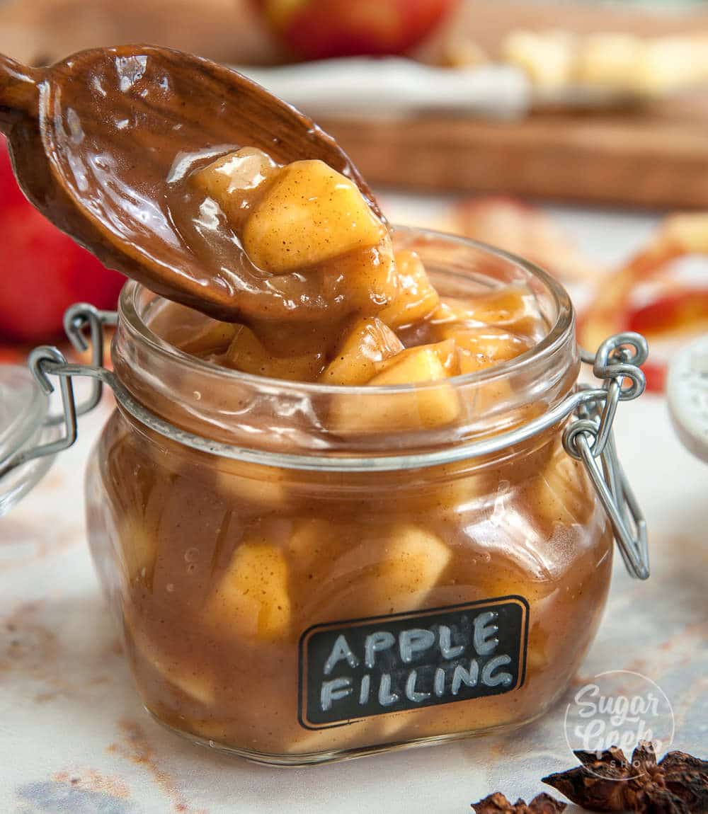 apple filling being spooned into a glass jar with apple filling label