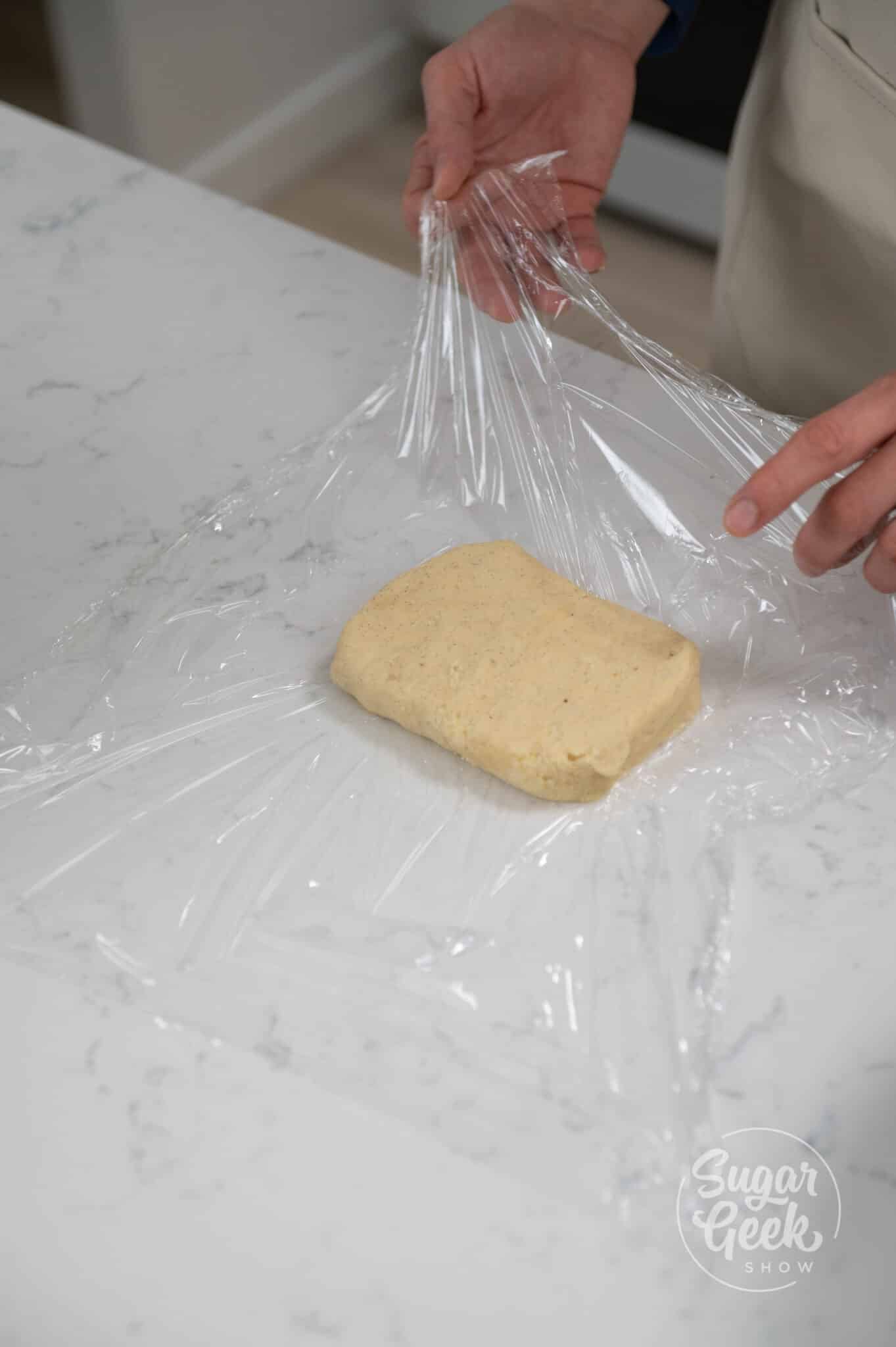 hands wrapping dough in plastic wrap.
