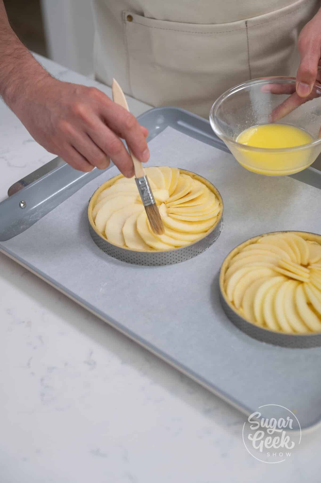 hands brushing melted butter on to apple tart.
