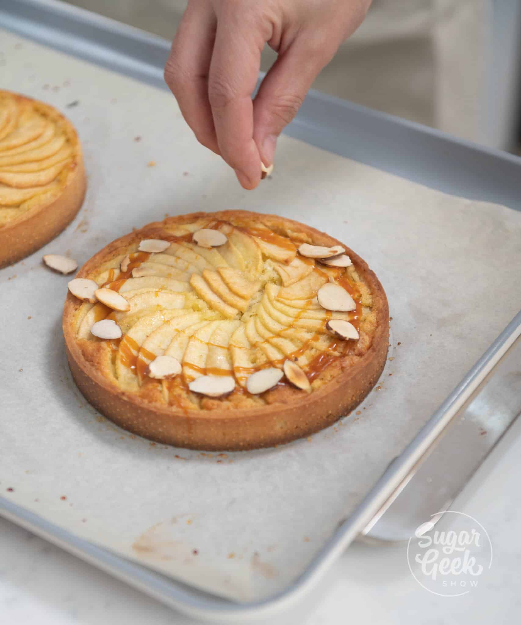 hands adding toasted almonds to tart.