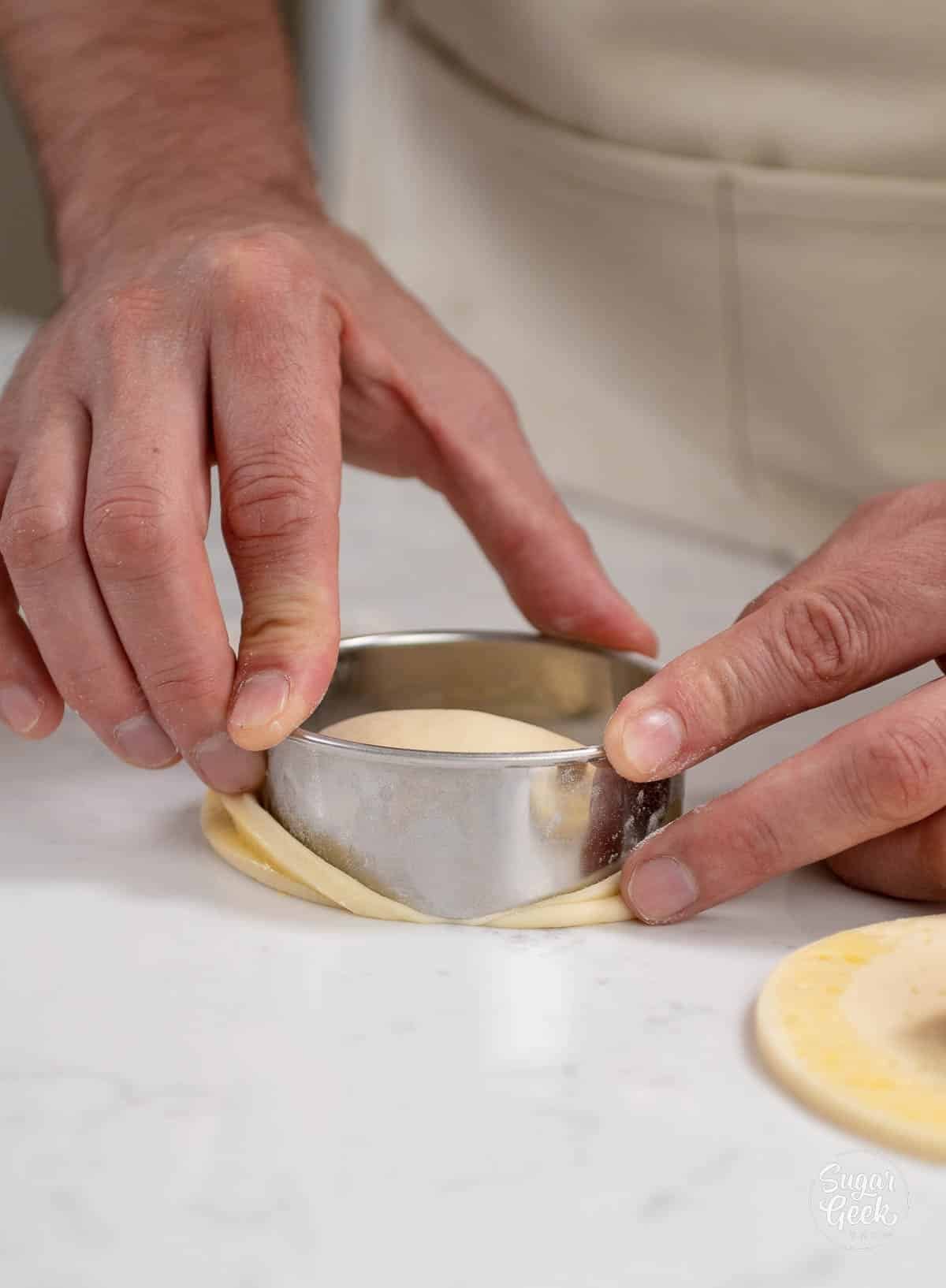 hands cutting off excess dough with a circle cutter.