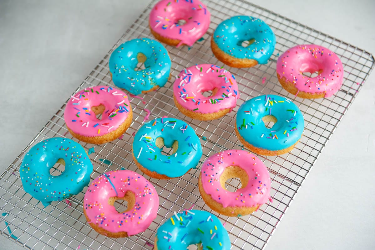 pink and blue glazed donuts with sprinkles on a cooling rack