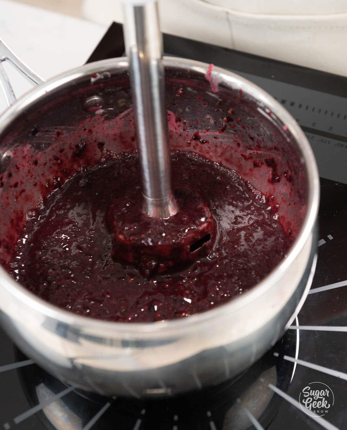 immersion blender blending frozen blackberries in a saucepan
