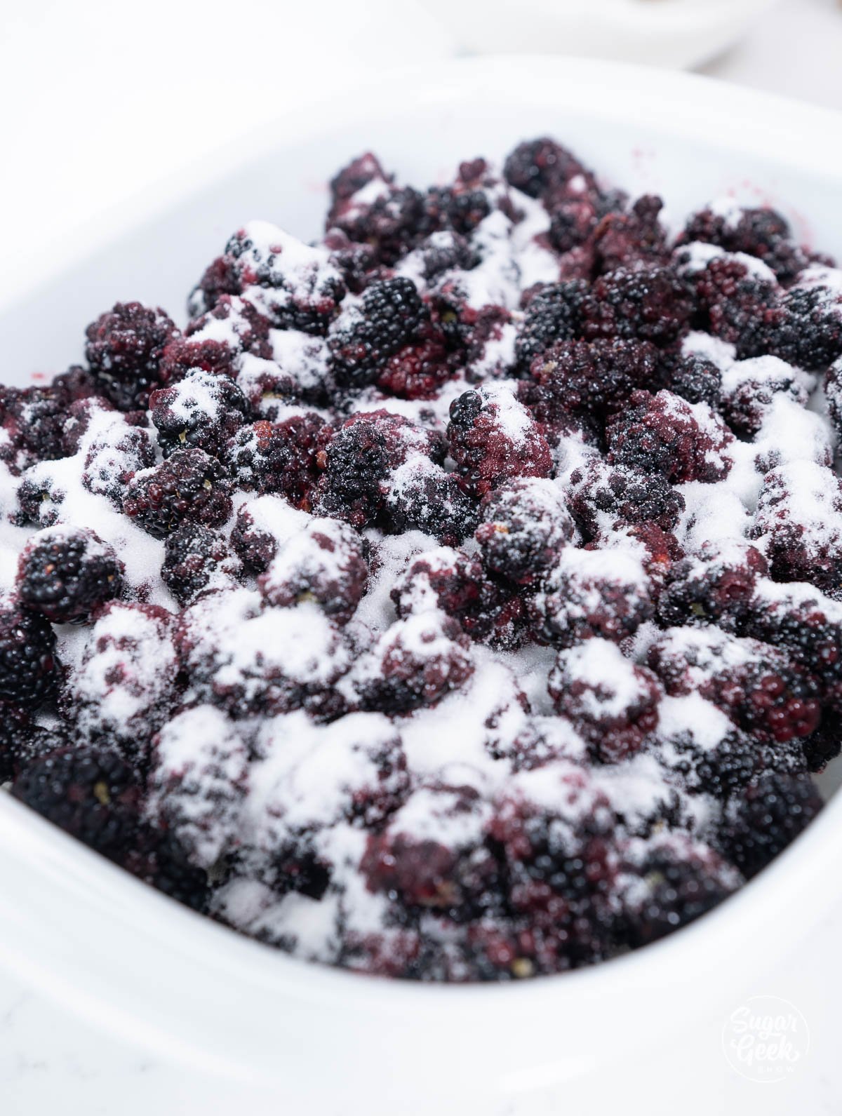 sugar sprinkled over blackberries in a white baking dish