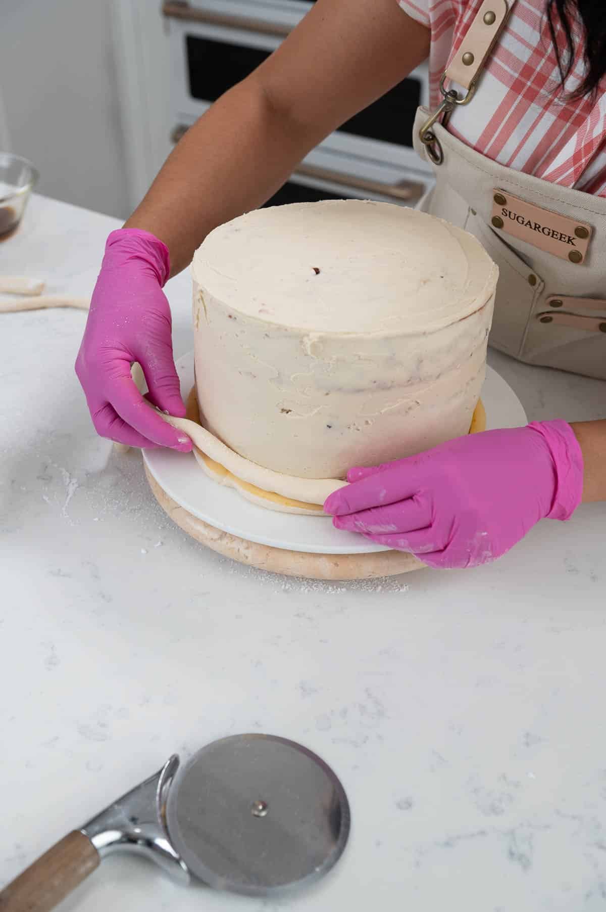 hands placing a strip of fondant against a cake