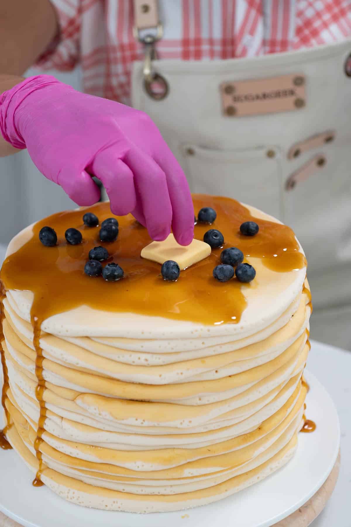 hand placing blueberries and fondant butter on top of a cake