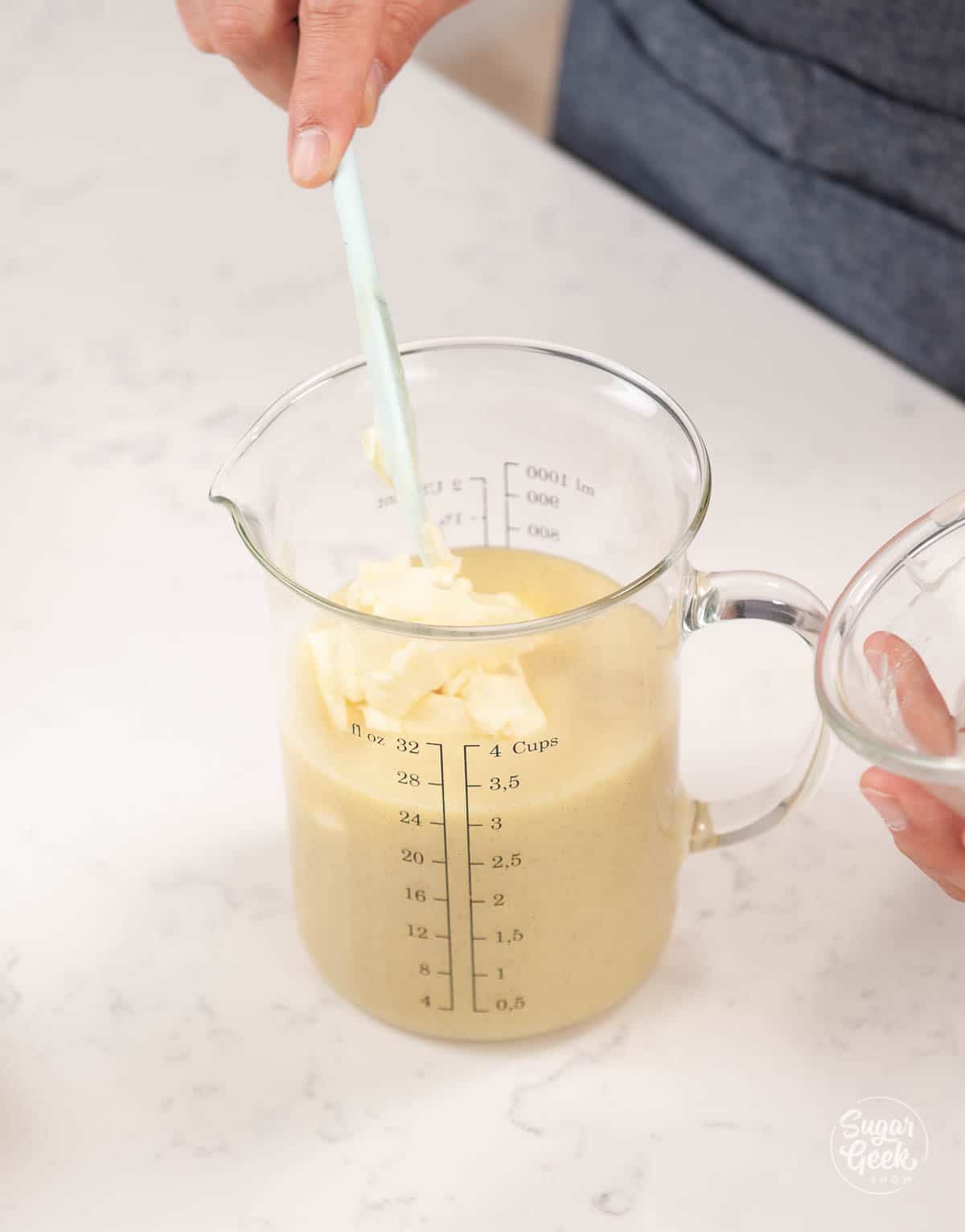 adding softened butter to ganache in a measuring cup