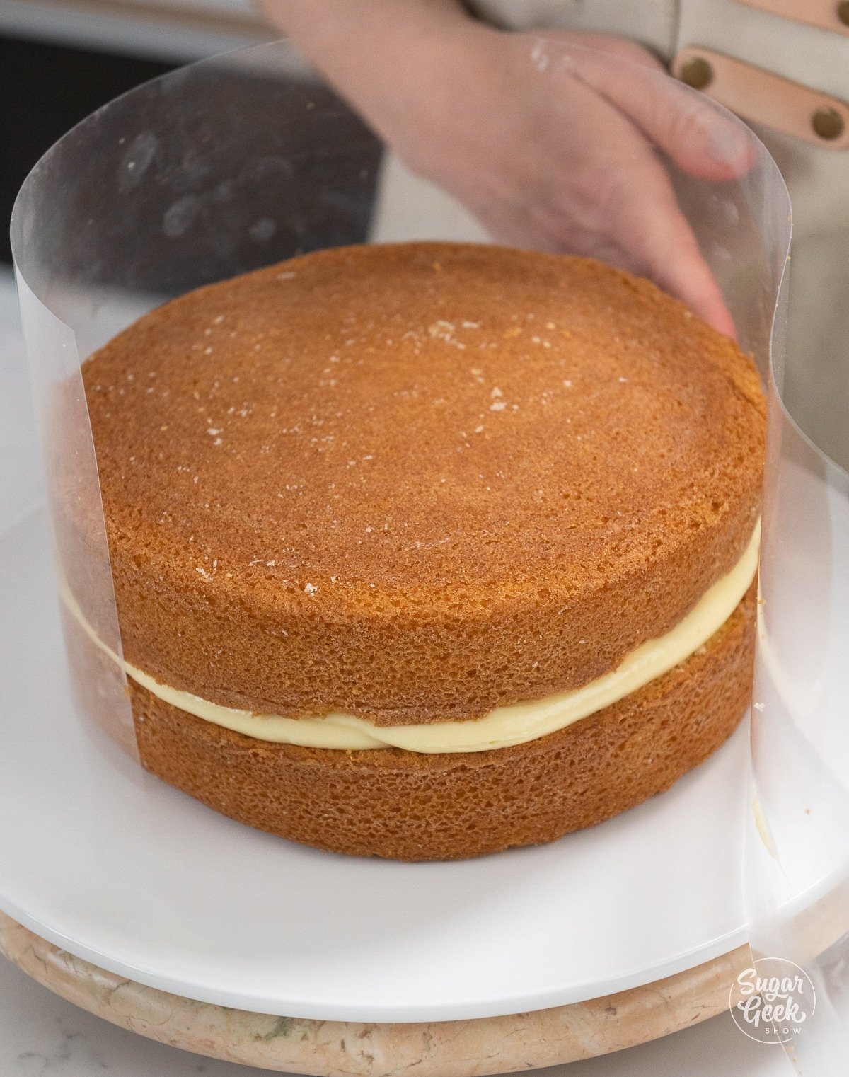 hand removing acetate collar from around filled and stacked cake.