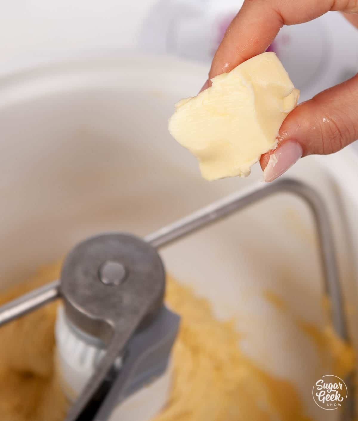 closeup of hand adding softened butter to brioche dough mixture