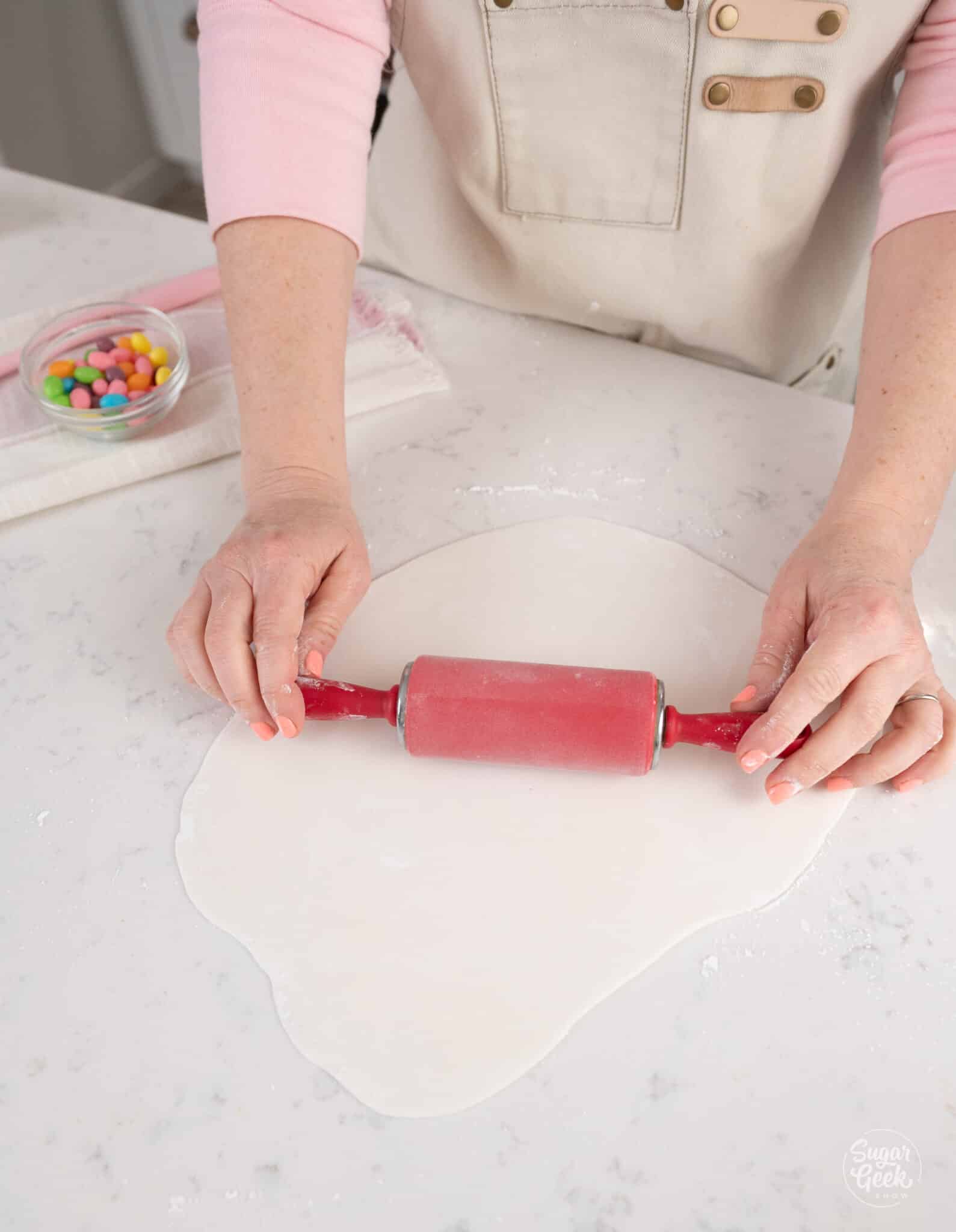 hands rolling out white fondant with a rolling pin