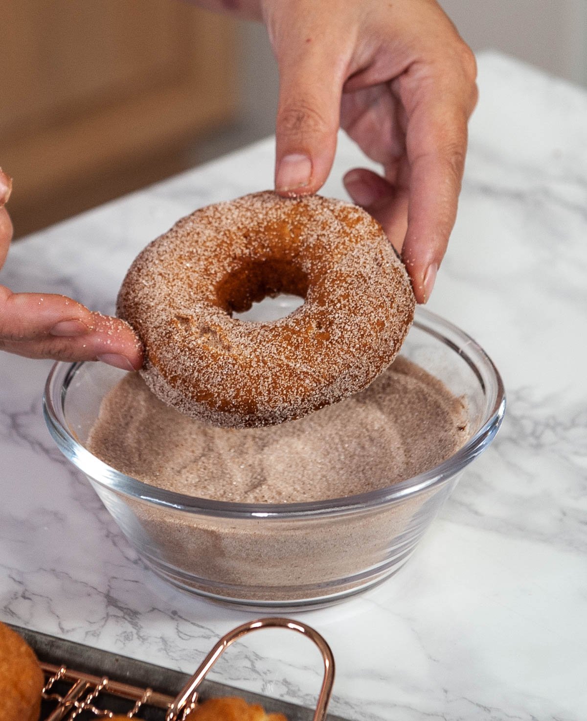donut being held above a glass bowl of cinnamon sugar