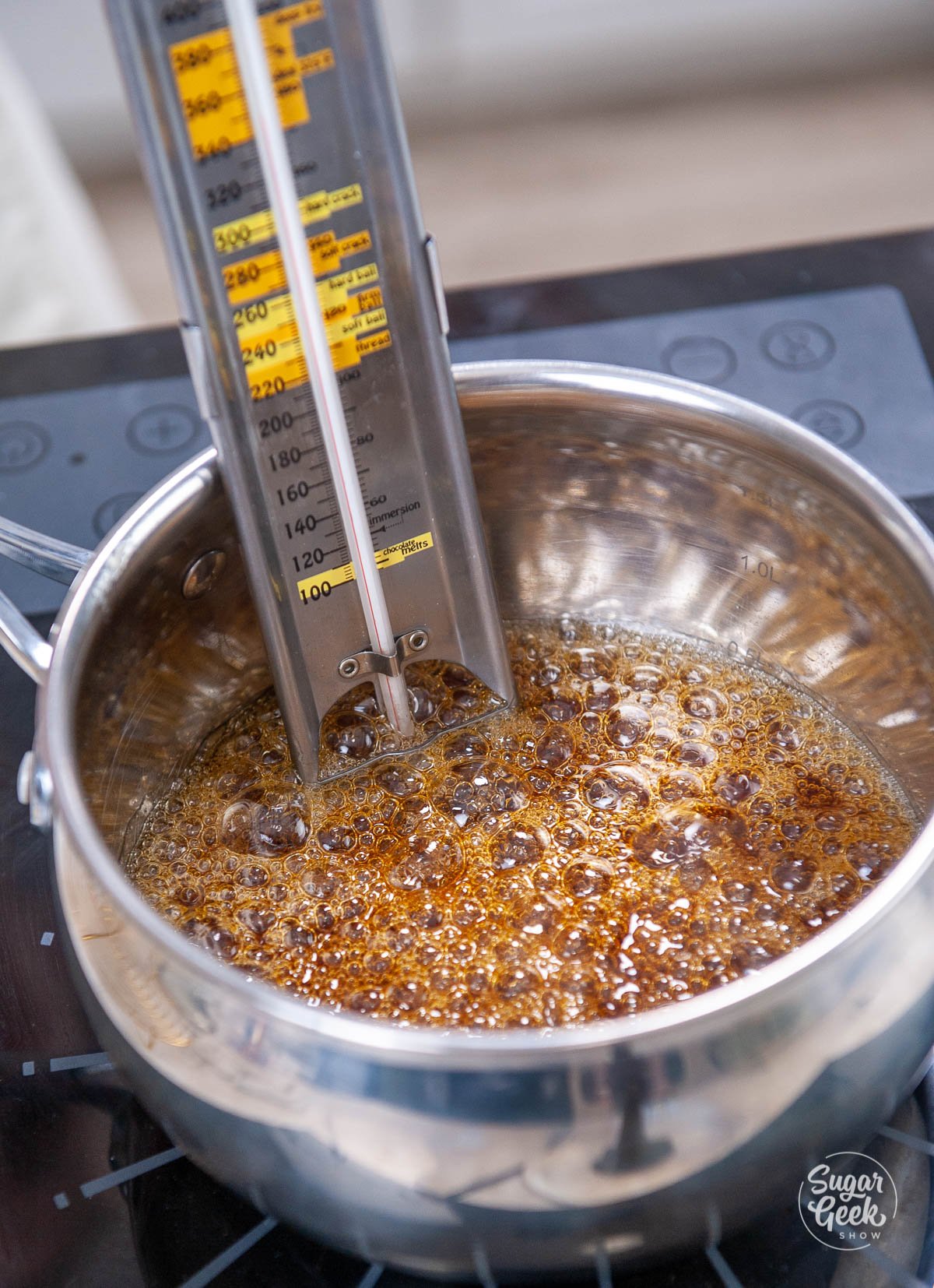 candy thermometer sitting inside pot of cooking caramel on stove top