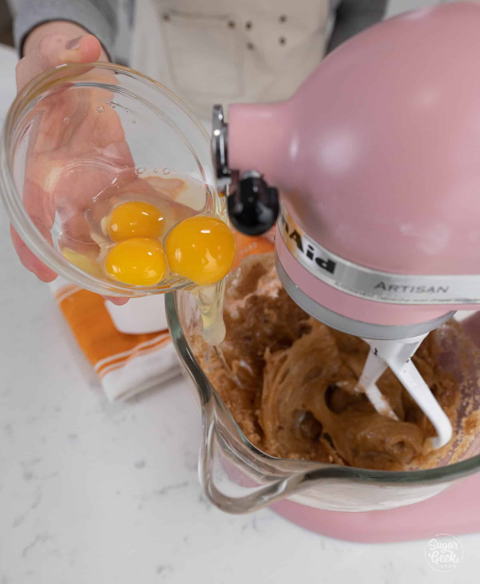 Hand adding a bowl of eggs to a stand mixer bowl