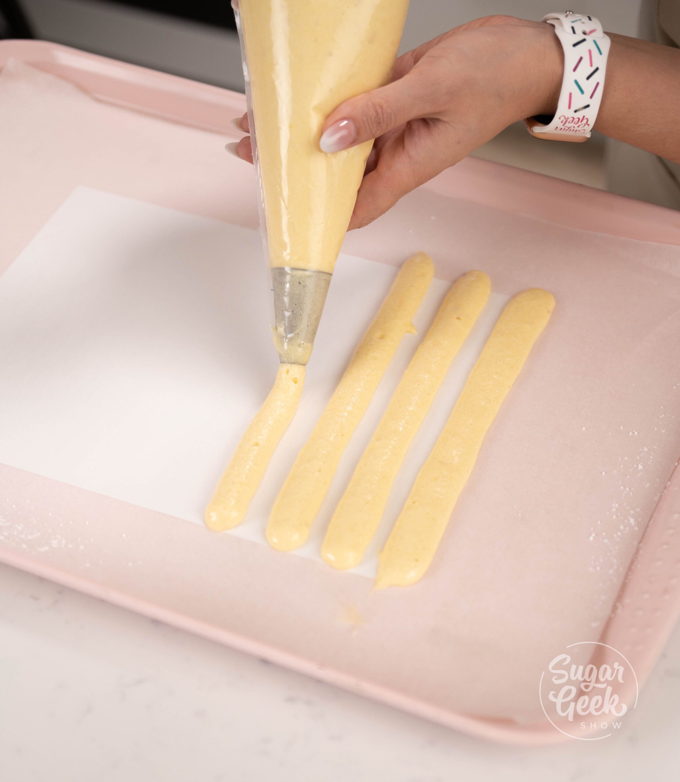 hand holding piping bag piping batter onto baking tray