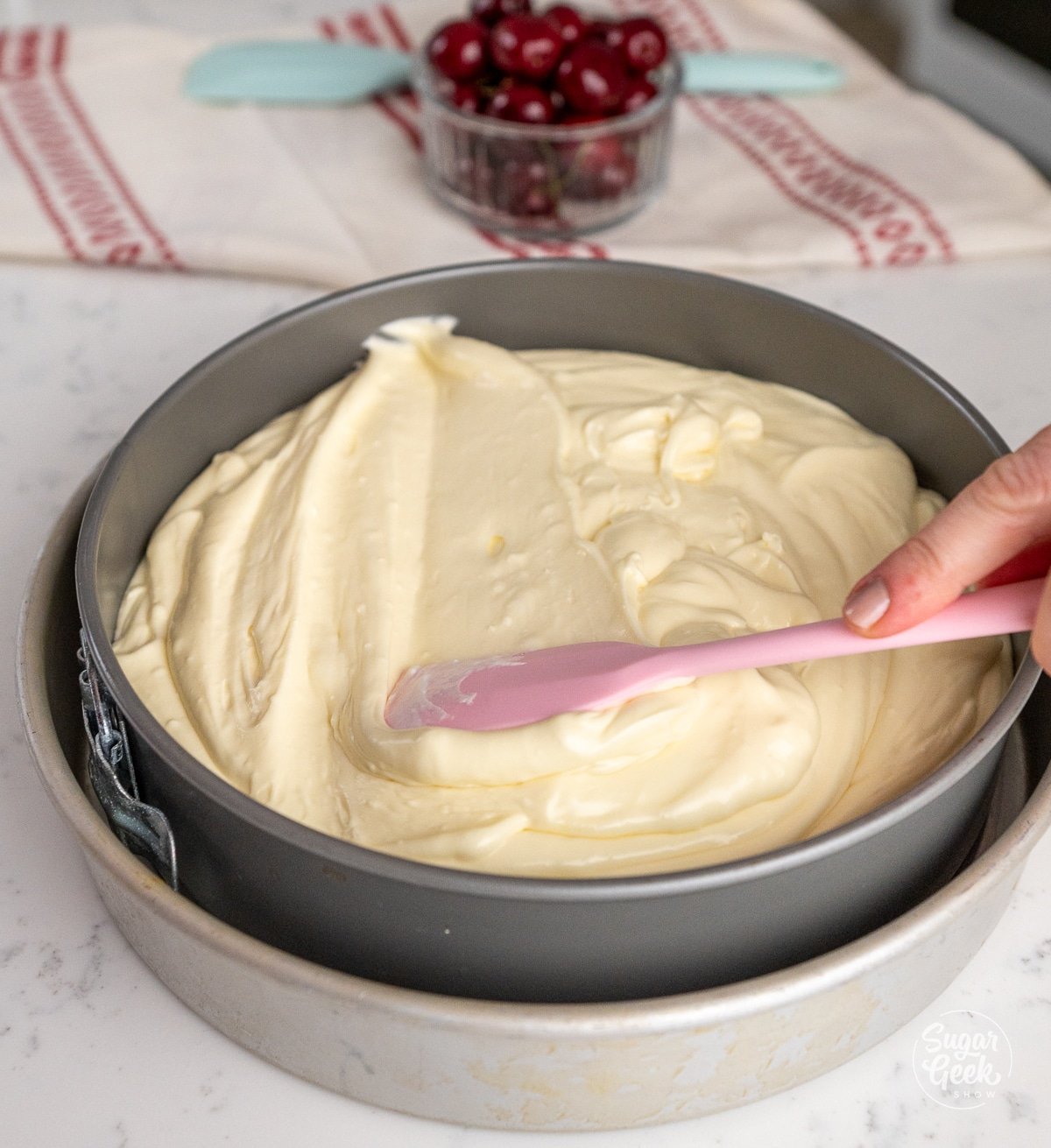 pink spatula smoothing cheesecake batter into a springform pan