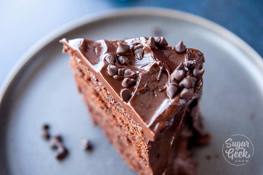 close up of a slice of chocolate cake with chocolate frosting and chocolate chips on top