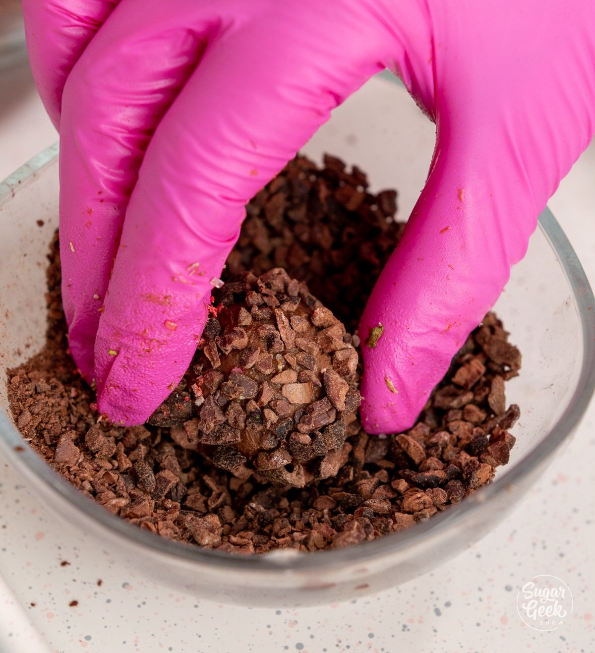gloved hand rolling a ganache truffle in cocoa nibs