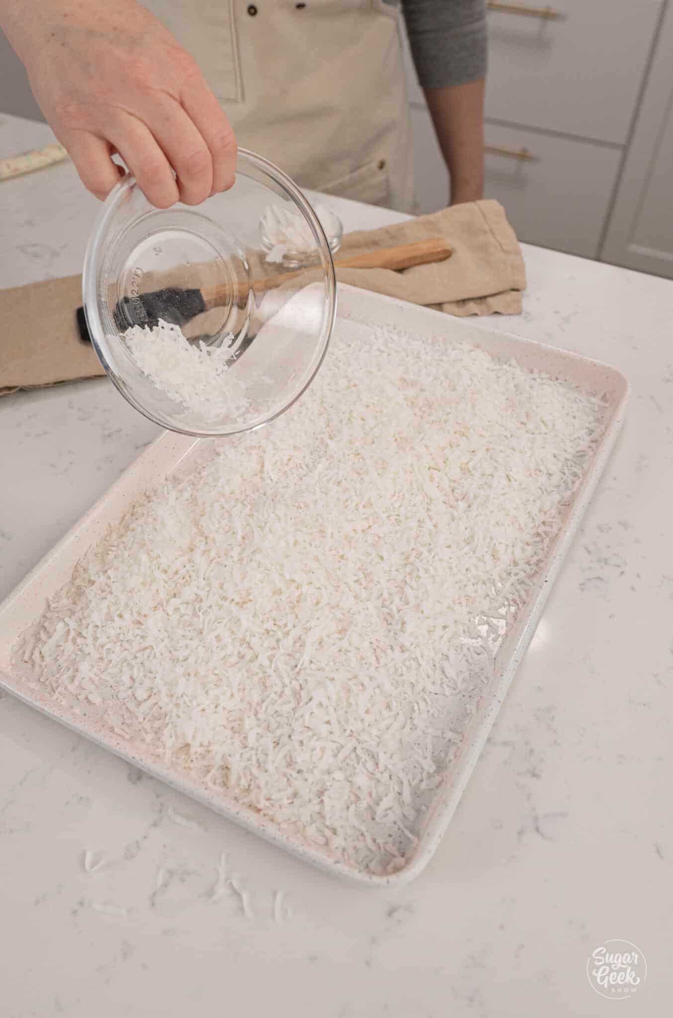 hand sprinkling coconut flakes on a sheet pan from a bowl