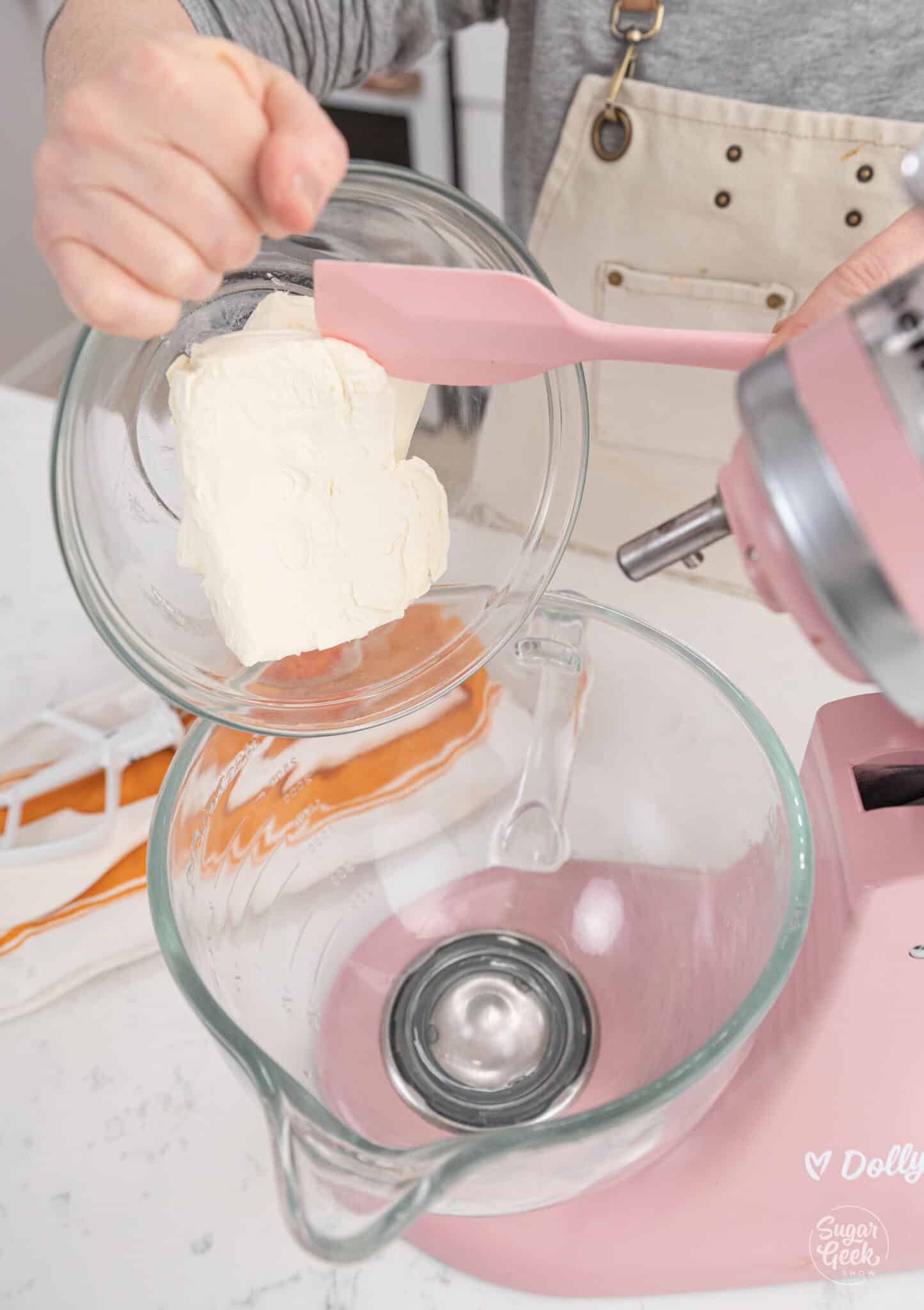 adding a bowl of cream cheese to a glass stand mixer bowl