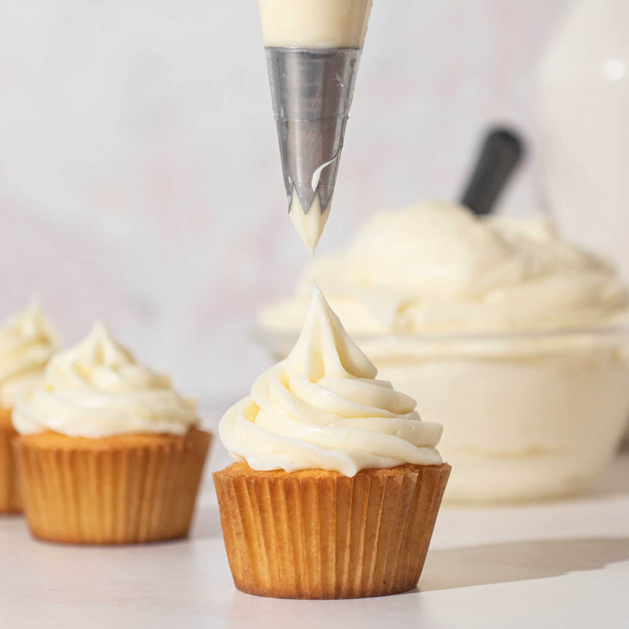 piping bag frosting a cupcake with cream cheese frosting