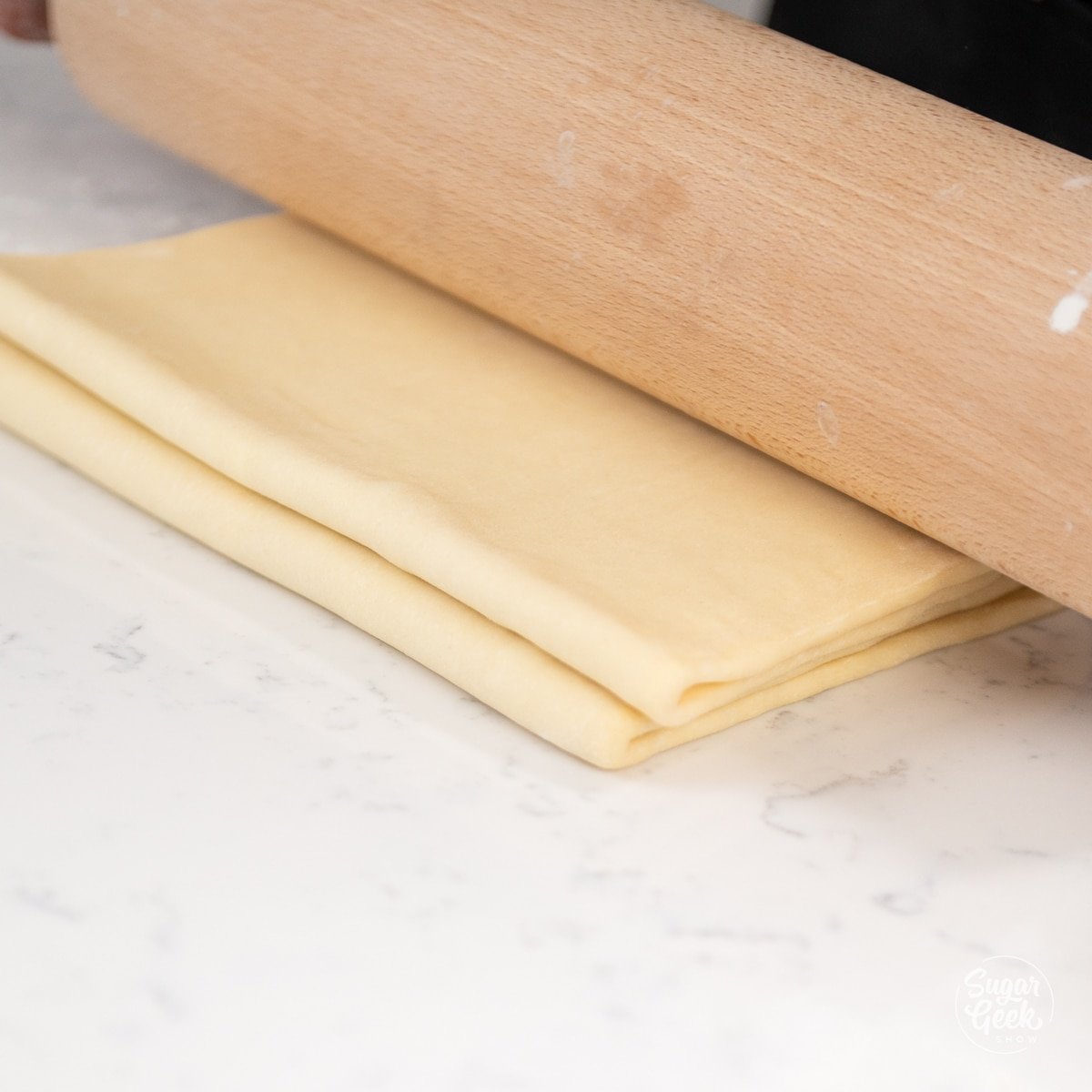 croissant dough folded in half with a wooden rolling pin on top