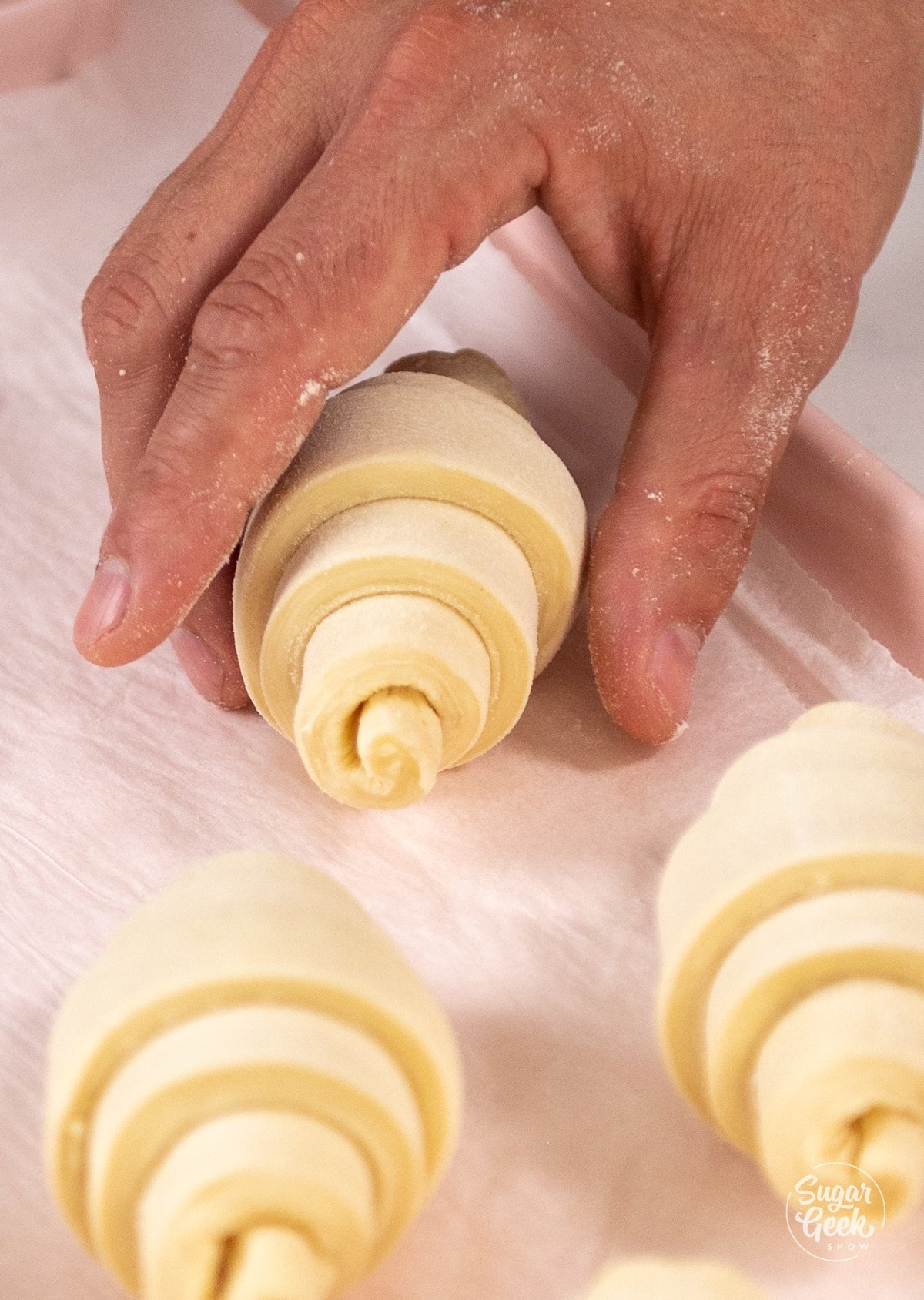 hand placing rolled croissants onto a baking sheet