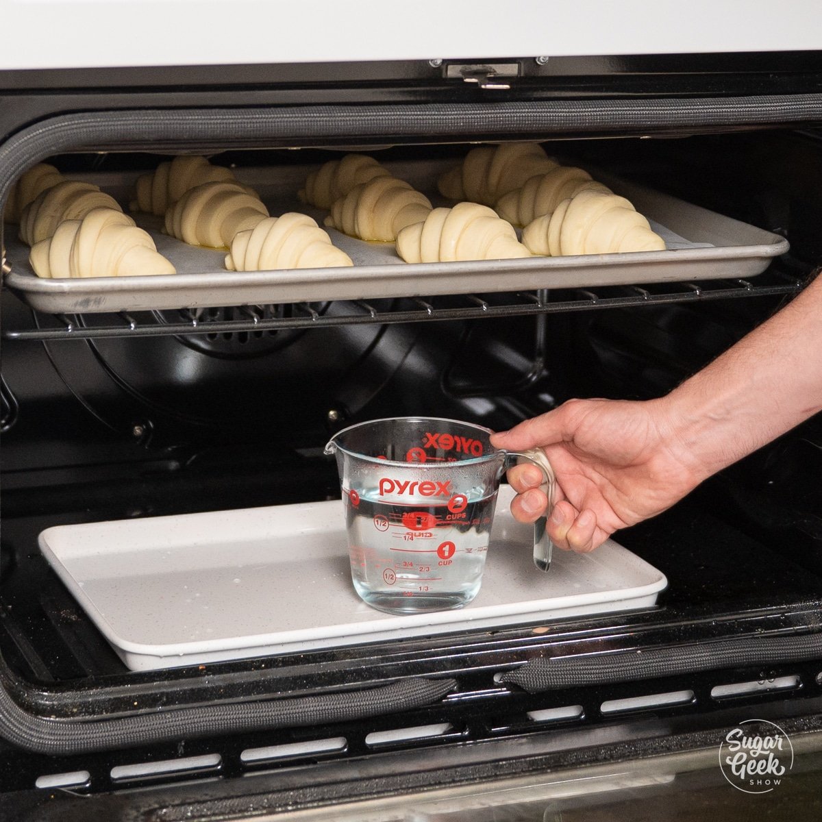 hand placing a measuring cup of water onto a baking sheet inside an oven