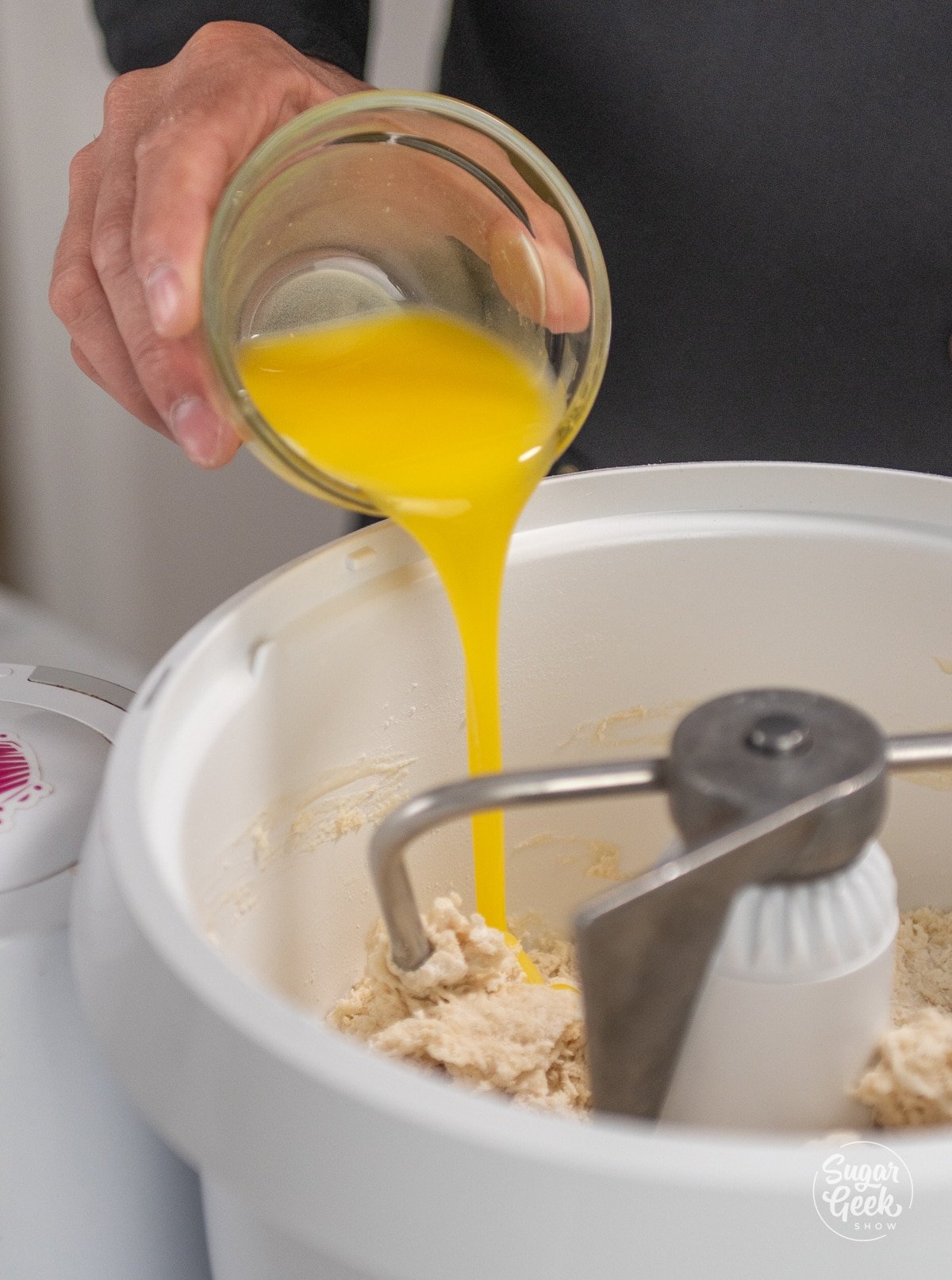 hand adding a bowl of melted butter into a white stand mixer bowl