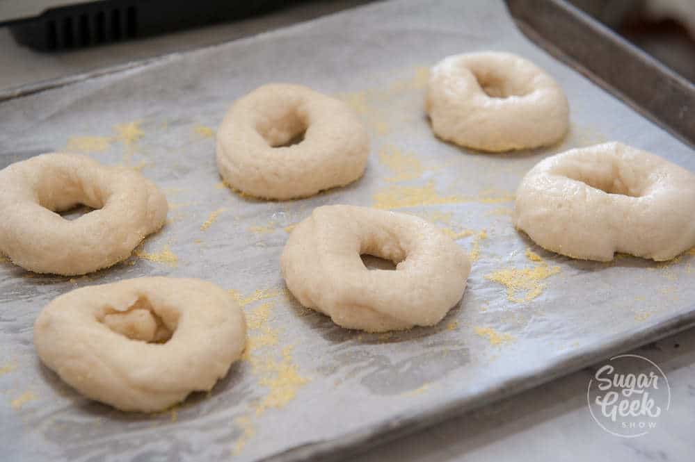 freshly boiled bagels on a sheet pan with parchment paper and cornflour