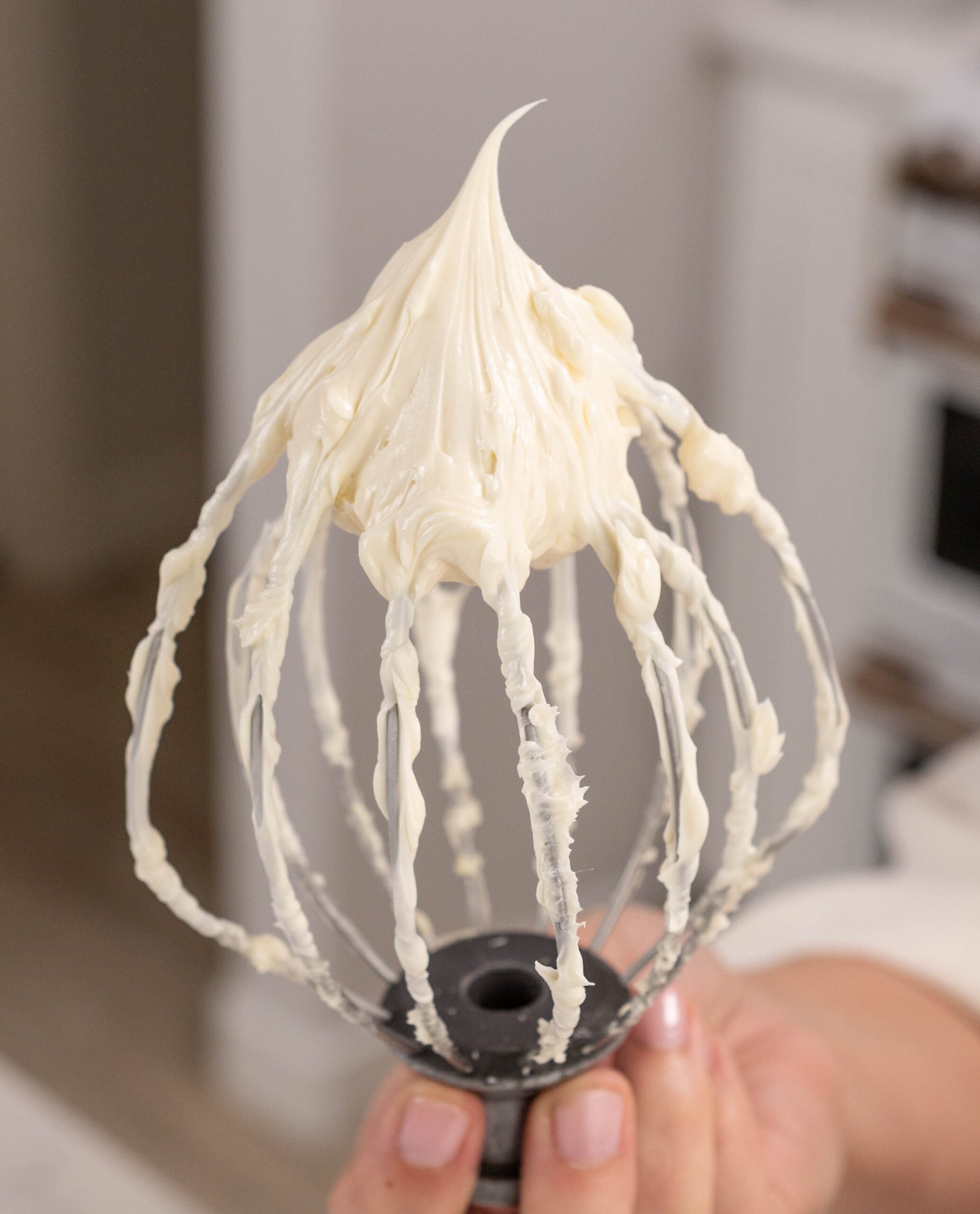 hand holding whisk covered in frosting