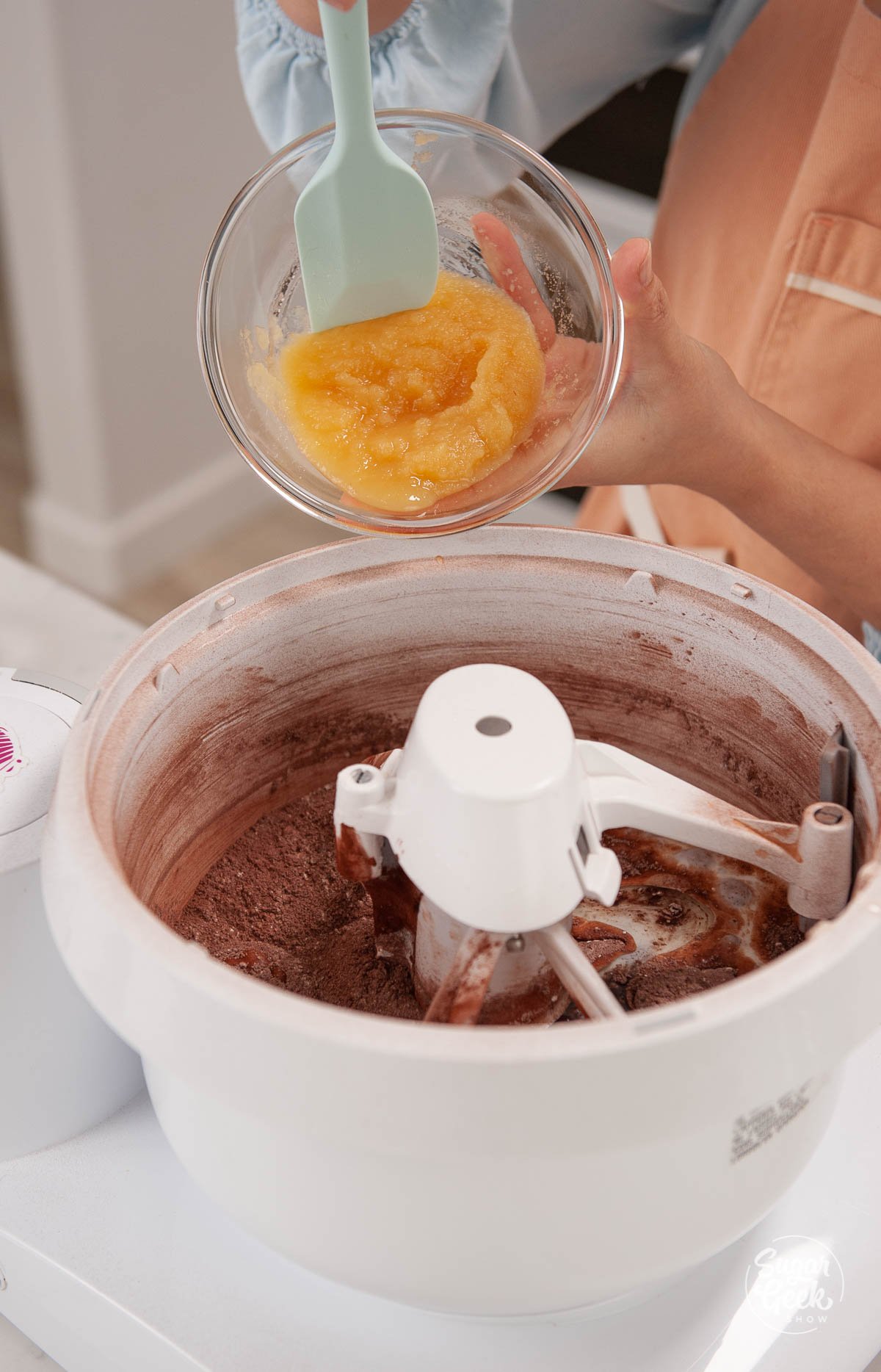 adding applesauce to chocolate cake batter in a mixing bowl