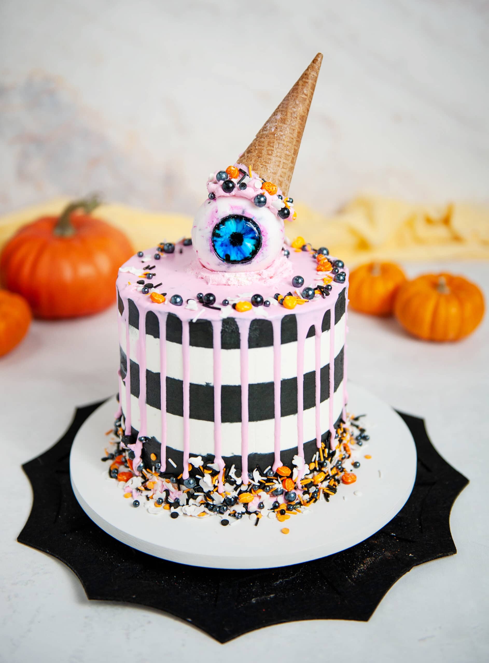 black and white striped cake with pink drip, gummy eyeball with ice cream cone on top