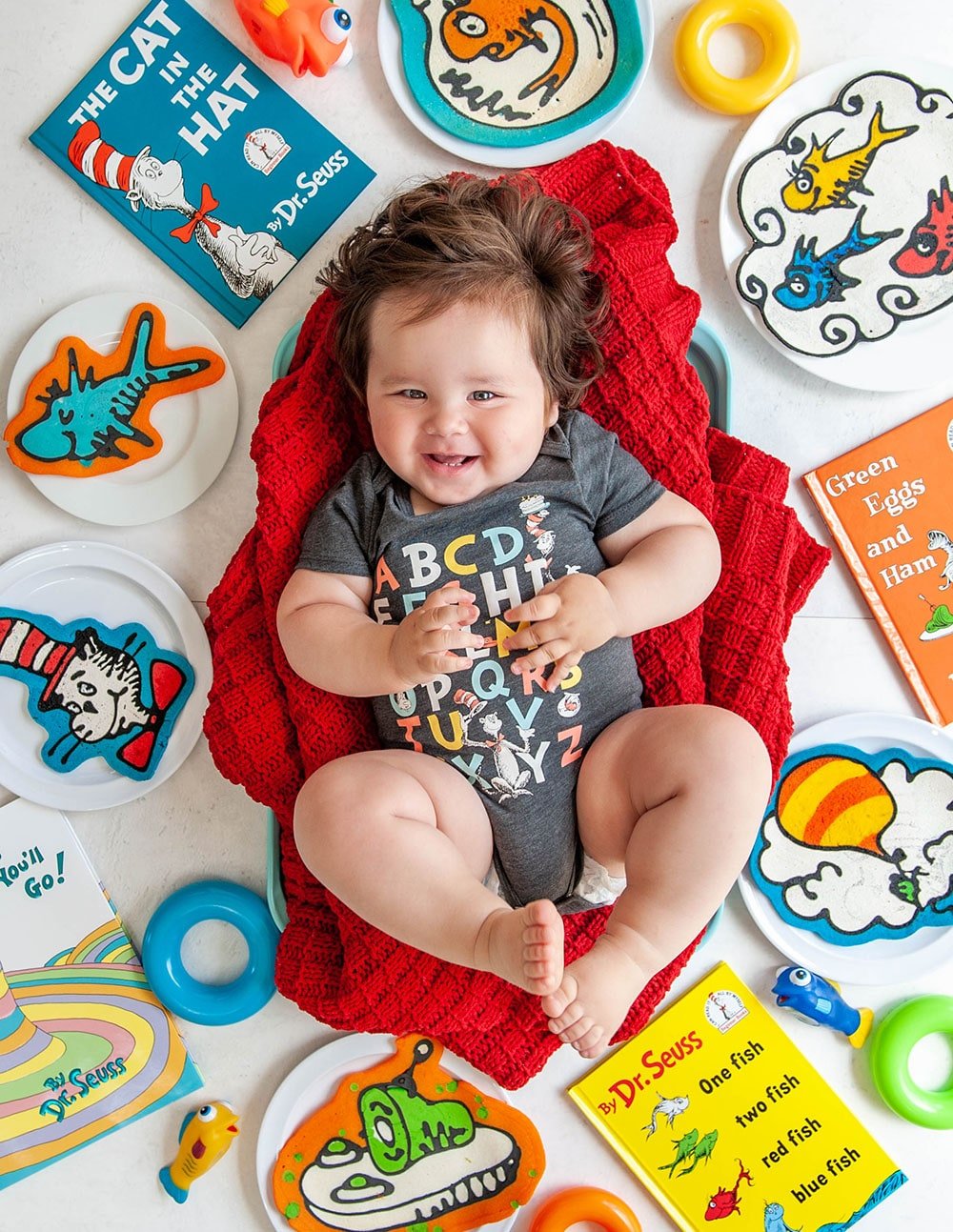 baby boy on red blanket with pancake art and dr seuss books surrounding him