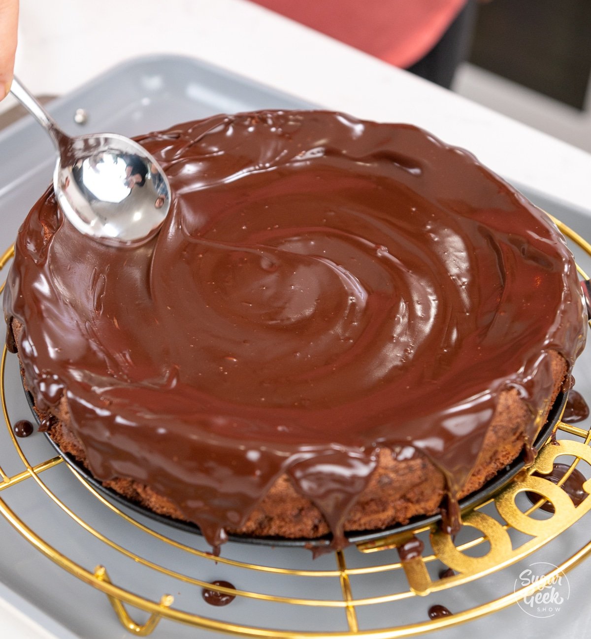 spoon smoothing out chocolate ganache on top of a flourless chocolate cake