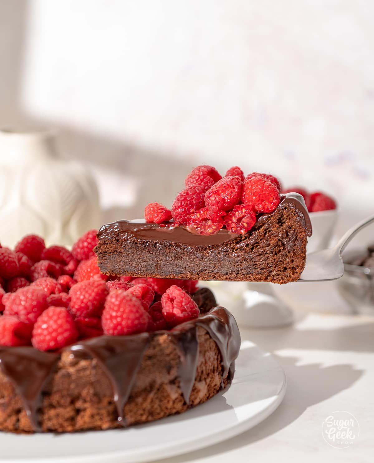 slice of flourless chocolate cake on a plate with raspberries on top lifted out of a cake