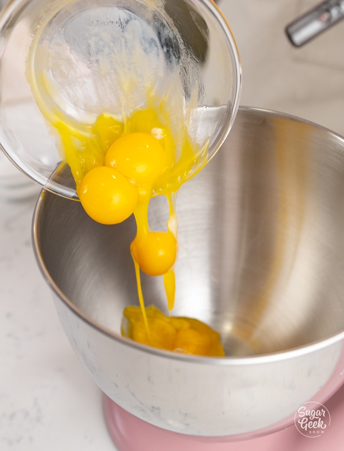 hand adding a bowl of egg yolks into a stand mixer bowl
