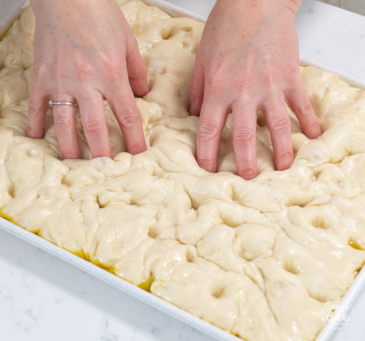 pressing indents into focaccia bread dough with fingertips