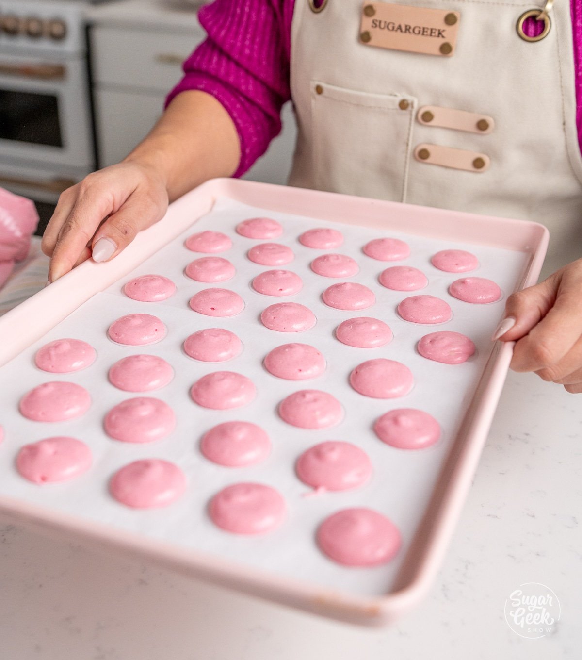 hands holding a baking sheet of unbaked macarons 6" above a table