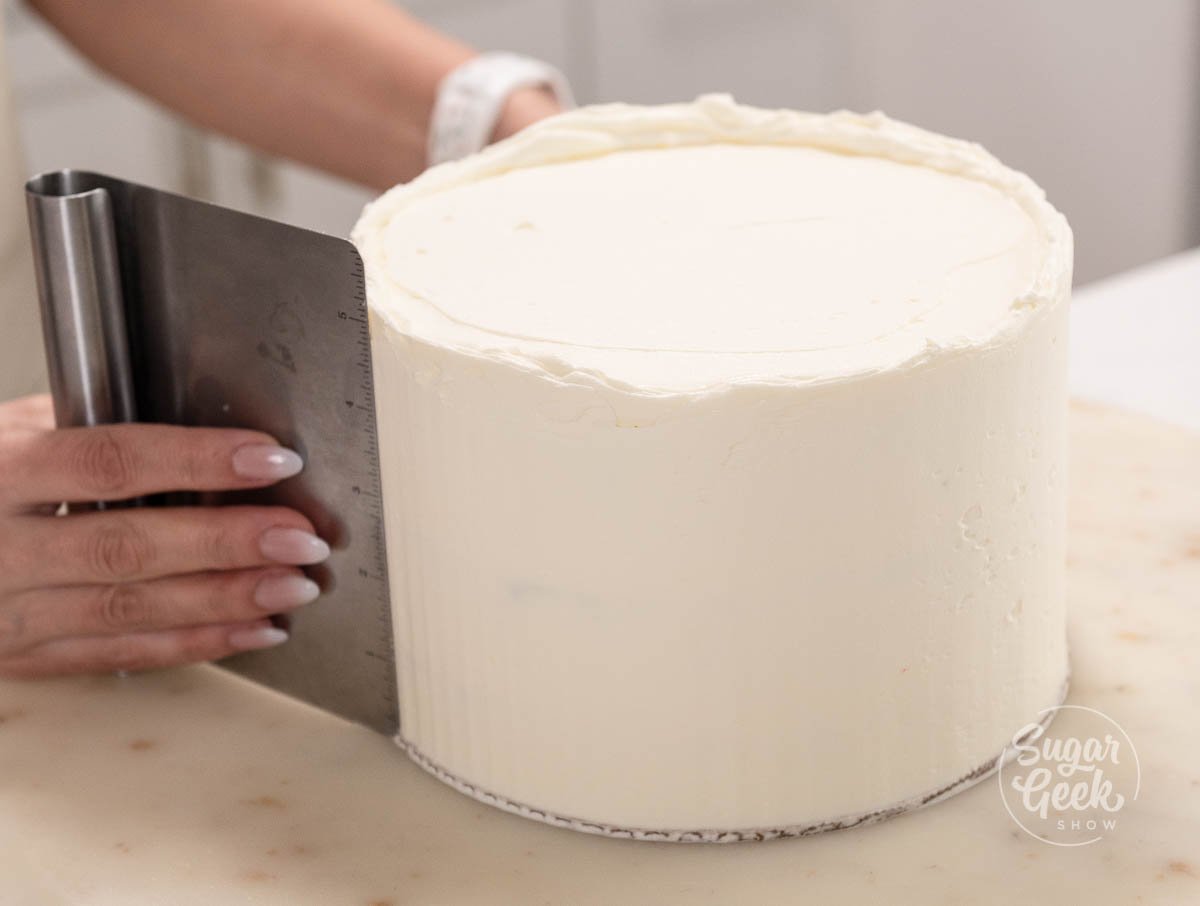 hand holding scraper while smoothing out cake