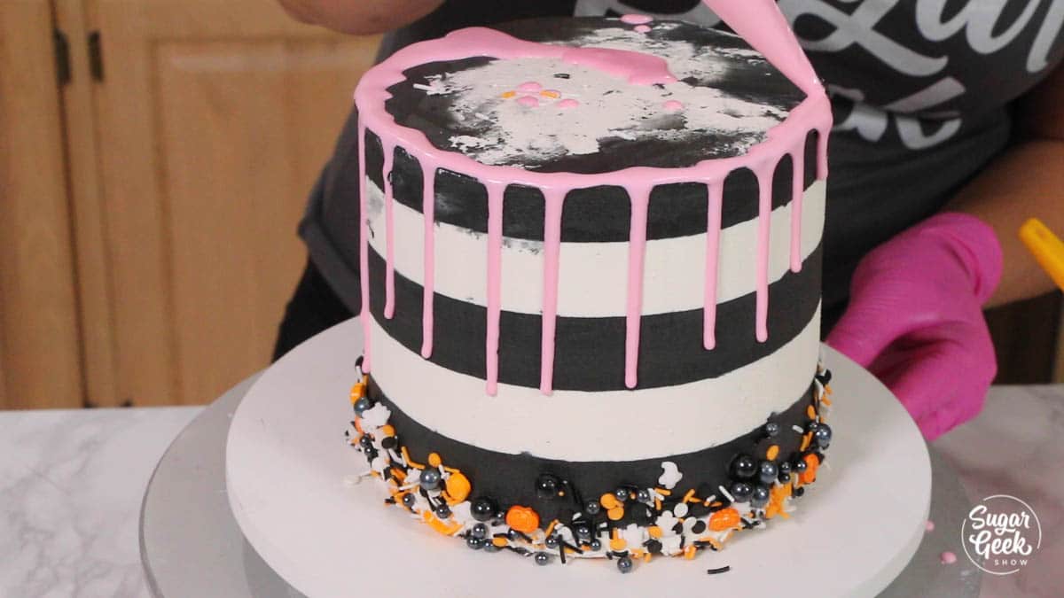 pink drip being added to black and white buttercream cake with halloween sprinkles