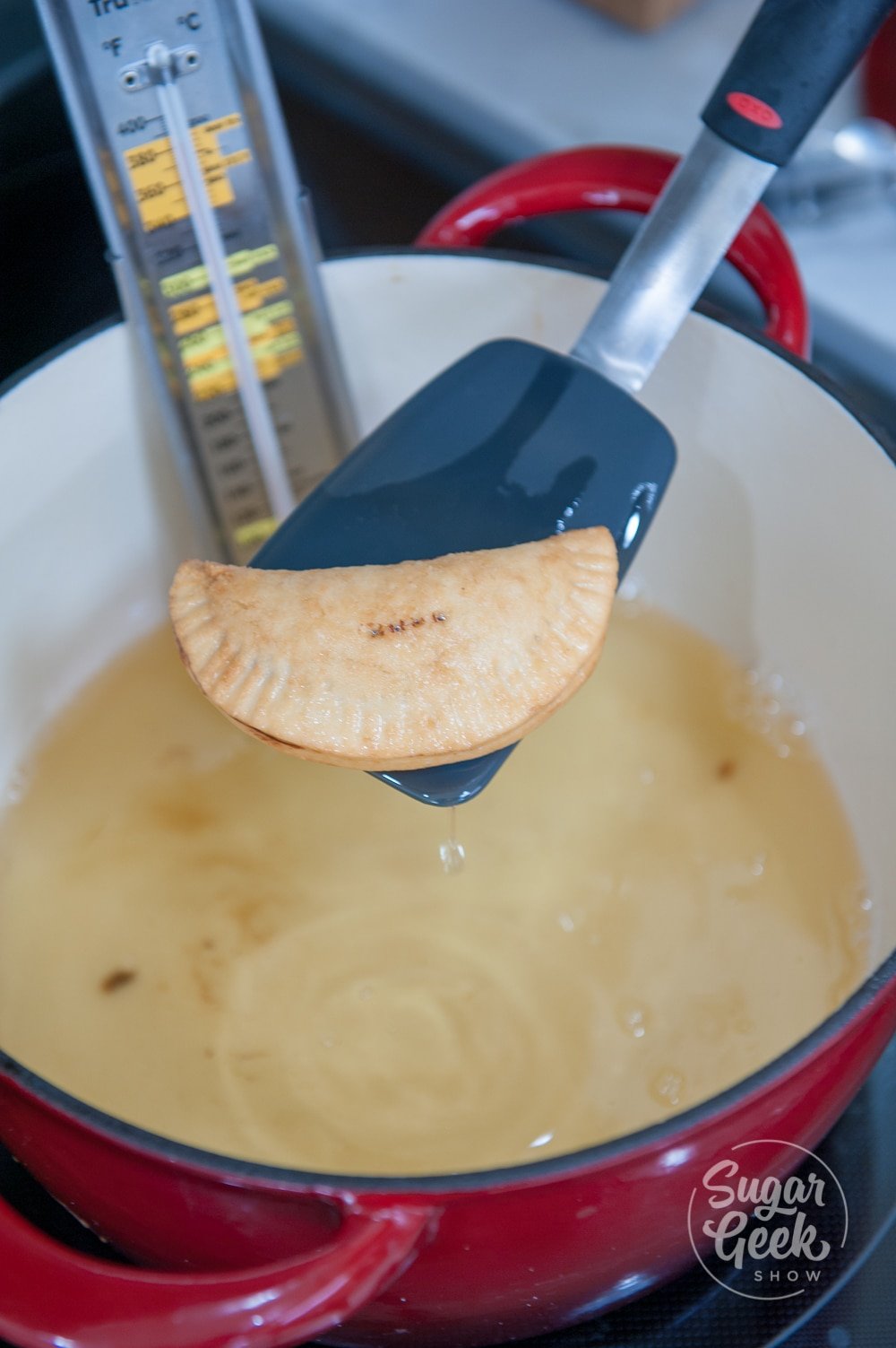 close up of a hand pie on a blue spatula above hot oil in a white pot