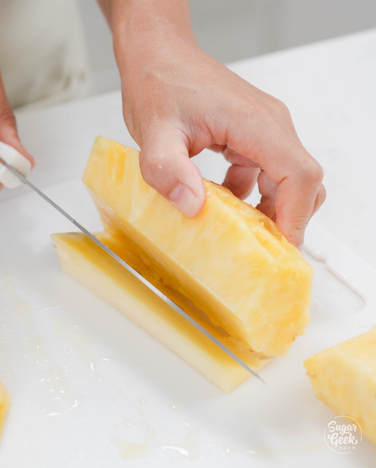 hands using knife to cut core out of pineapple. 