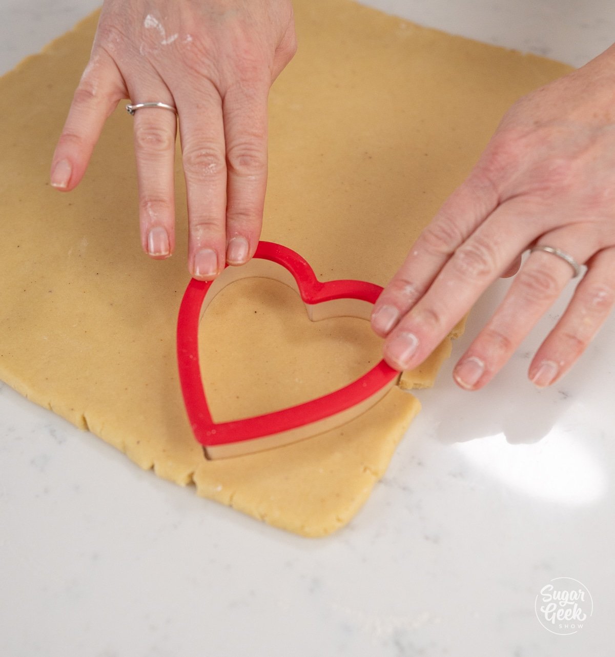 hands using heart cutter to cut heart shaped cookies.