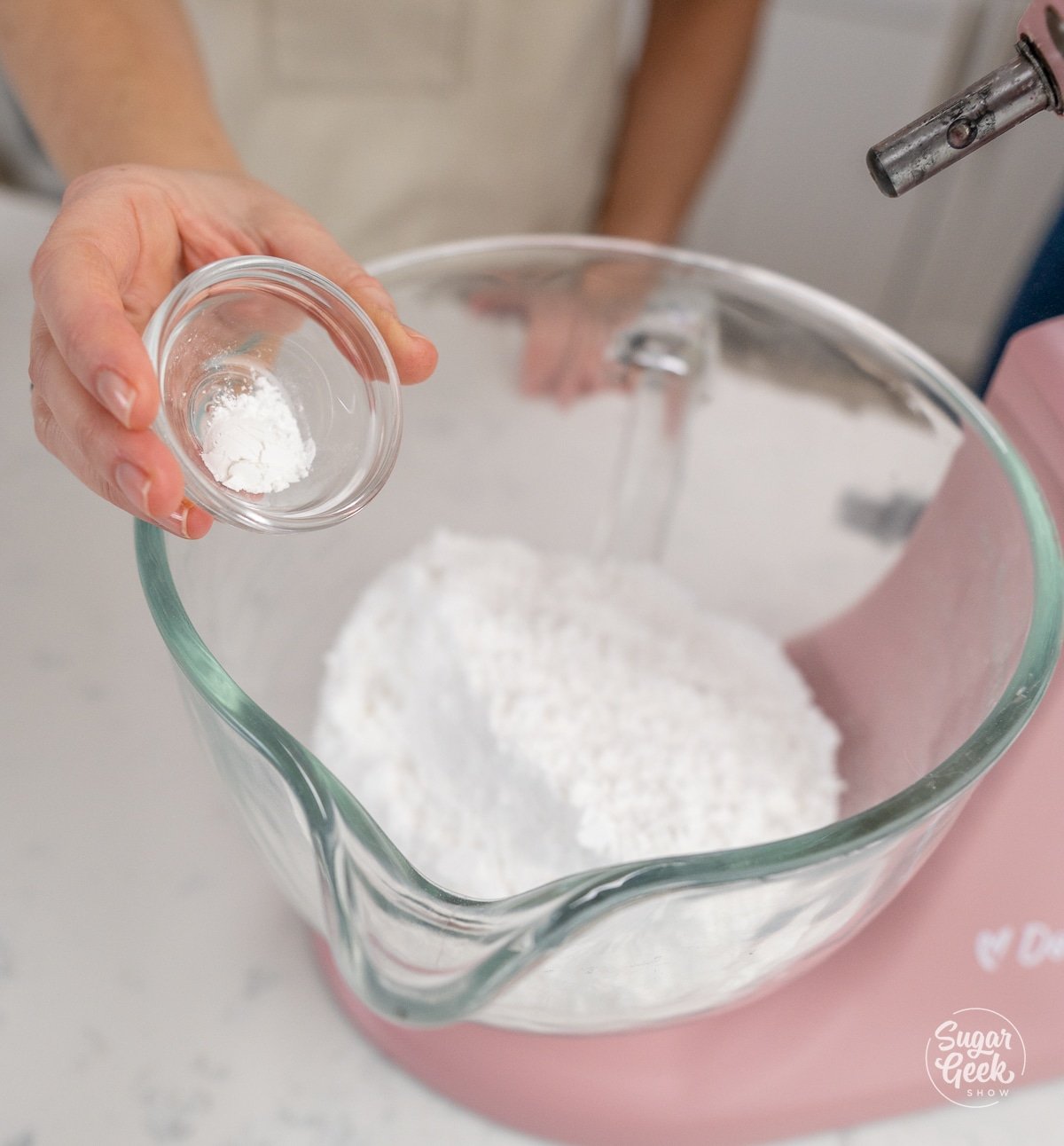 hand adding dry ingredients into stand mixer bowl. 