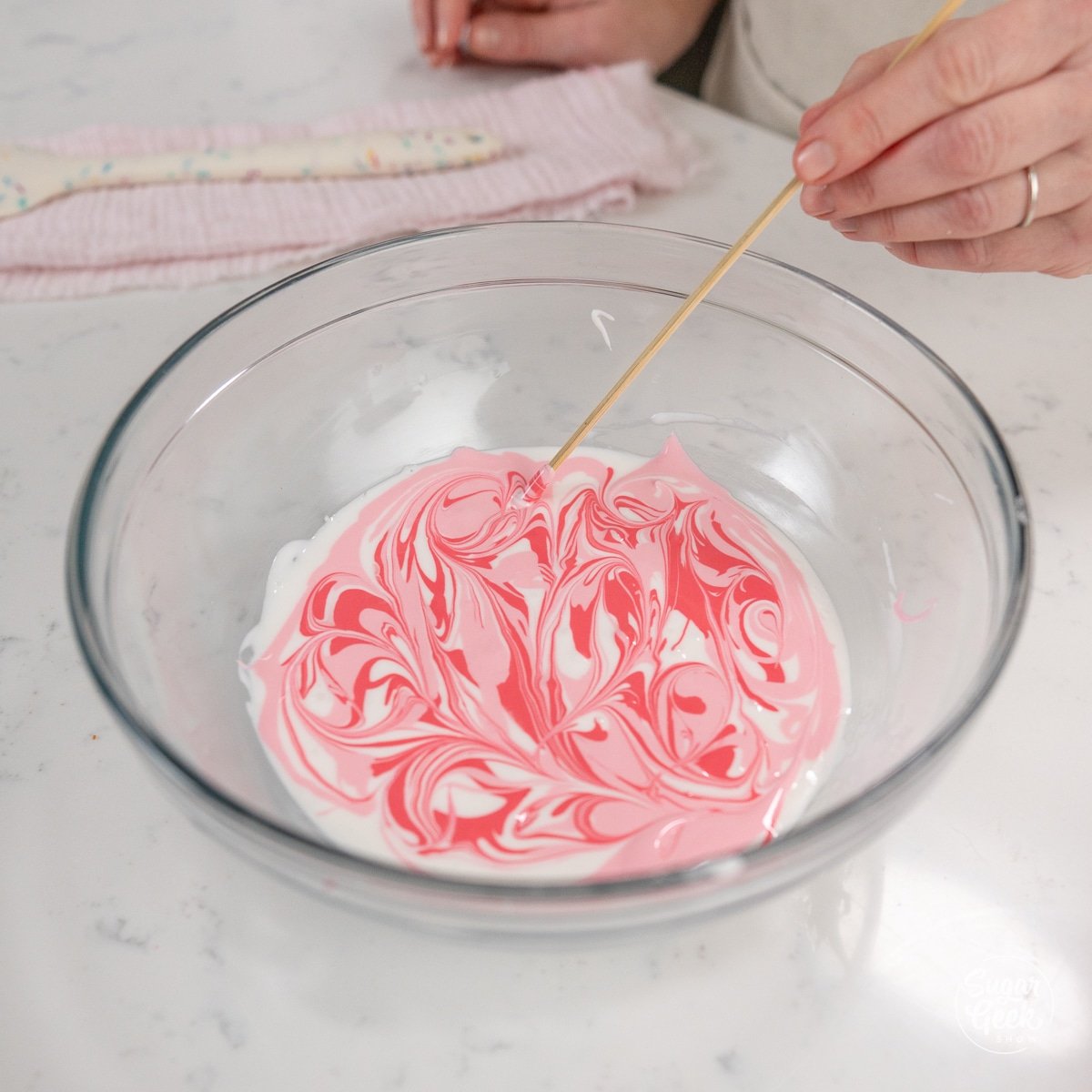 hand using skewer to create marble effect into royal icing. 