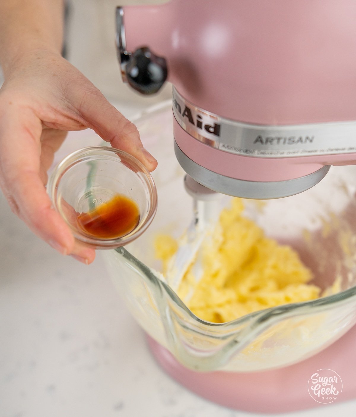 hand adding bowl of vanilla into dough mixture.