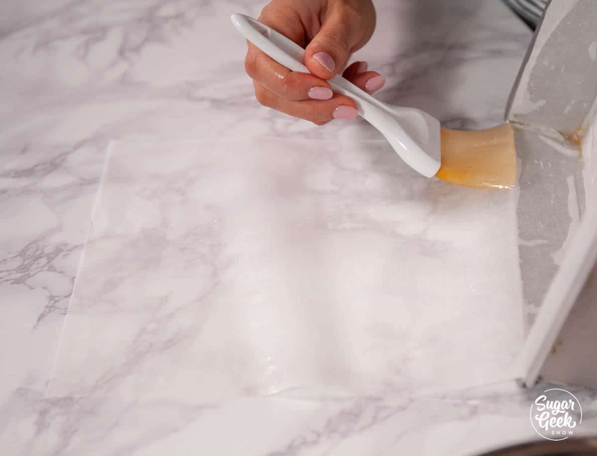 hand brushing oil onto parchment paper with a pastry brush