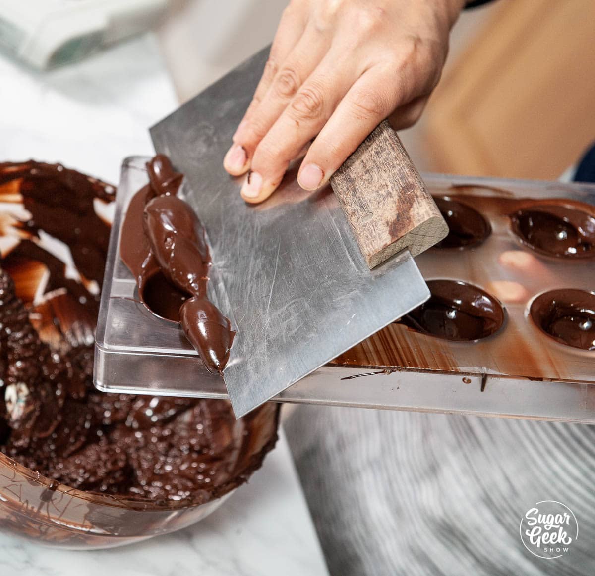 scraping excess chocolate off the mold with a bench scraper